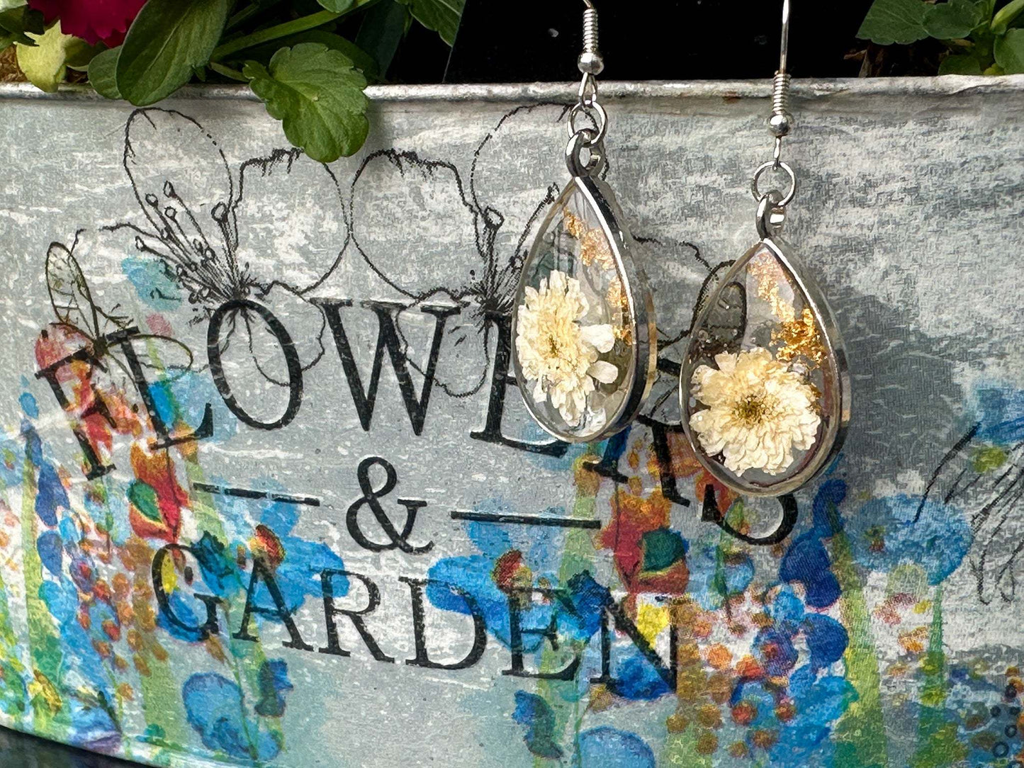 A teardrop silver frame is filled with real dried white flowers and flakes of gold foil are a romantic set of earrings