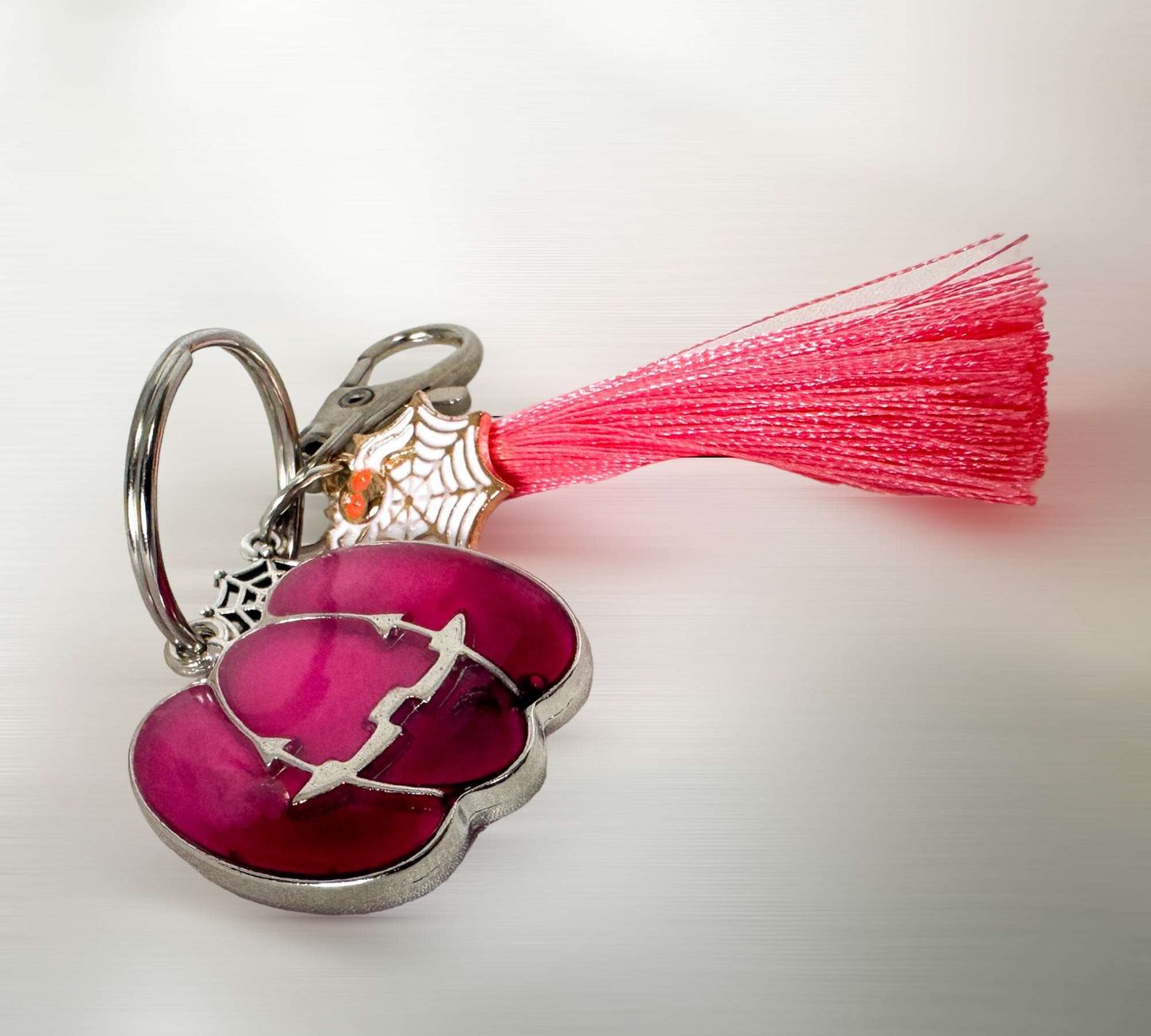 A Two Tone Pink Glow in the Dark Pumpkin shaped Keychain with a pink tassel and Halloween charms