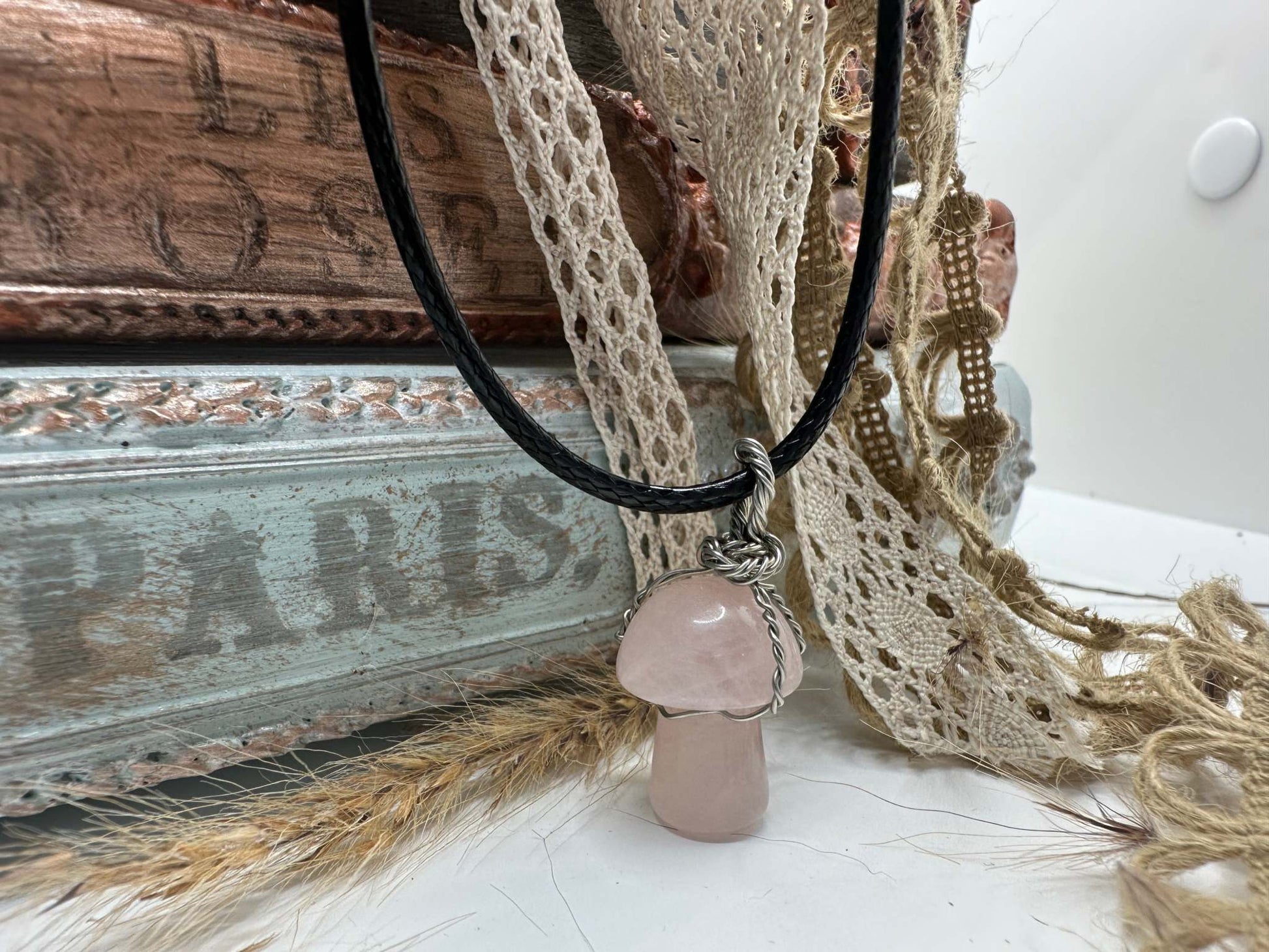A Rose Quartz Mushroom Shaped Gemstone Necklace hangs from a black leather cord