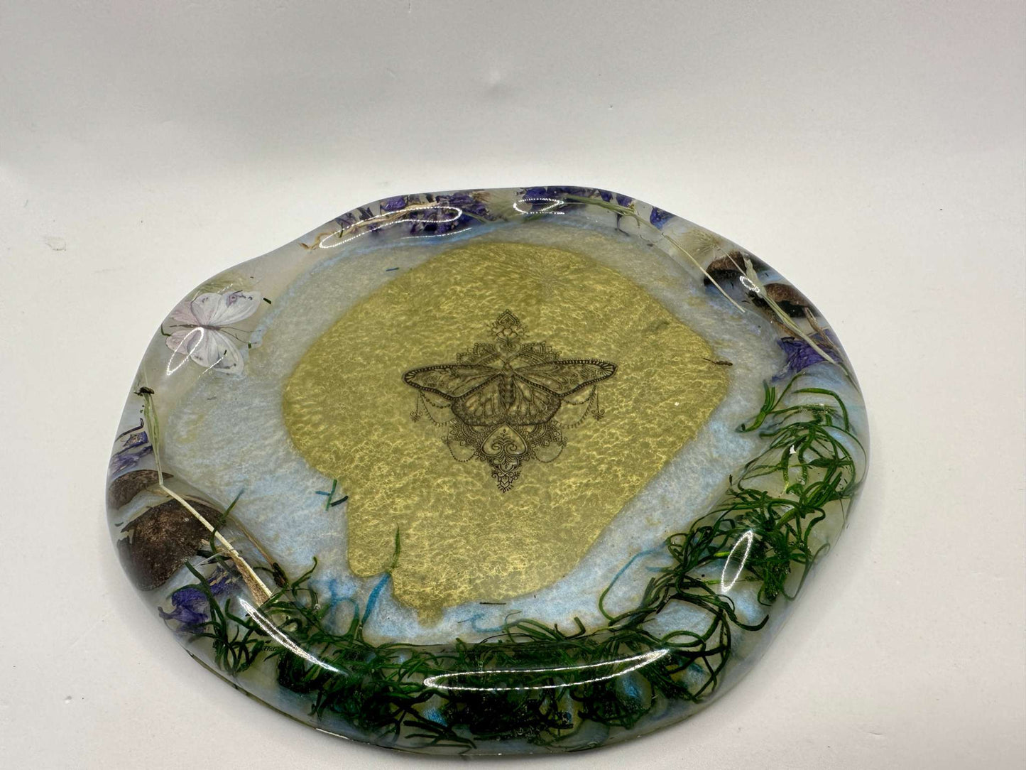A round Resin Tray filled with real dried flowers with a soft white/blue and green background with  butterflies as an accent