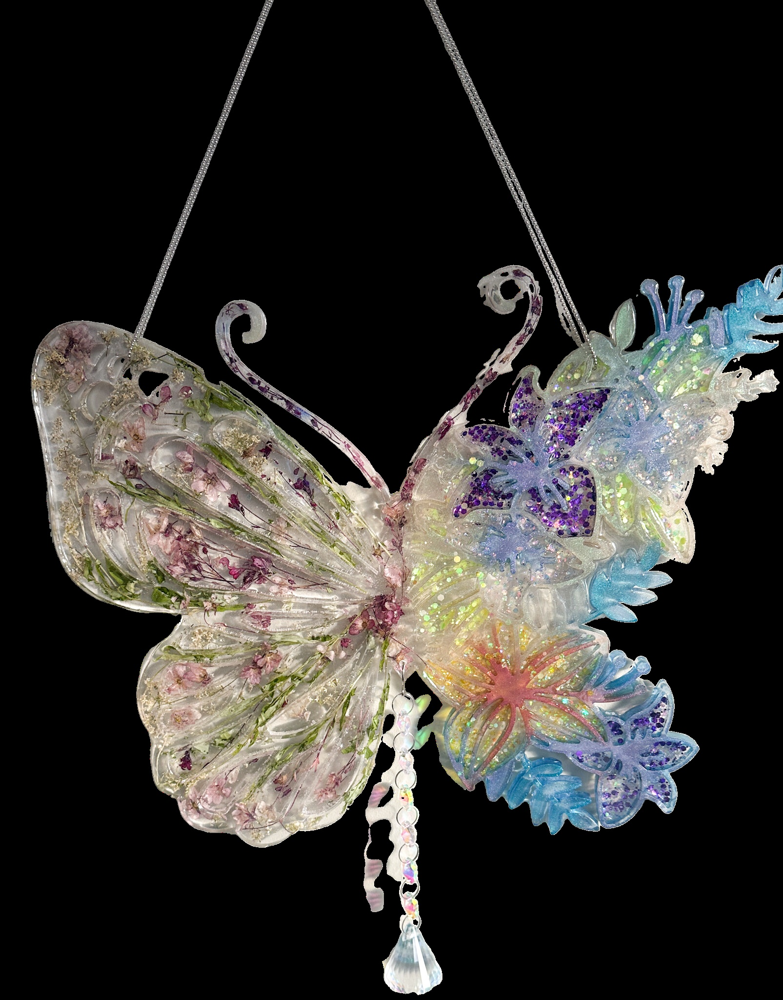 A large Butterfly created with Epoxy Resin with one half filled with dried flowers and the other half filled with glitter and bright colours. A prism crystal ball pendant hangs from the butterfly